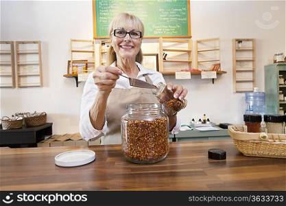 Portrait of a happy female employee pouring spice with scoop in jar