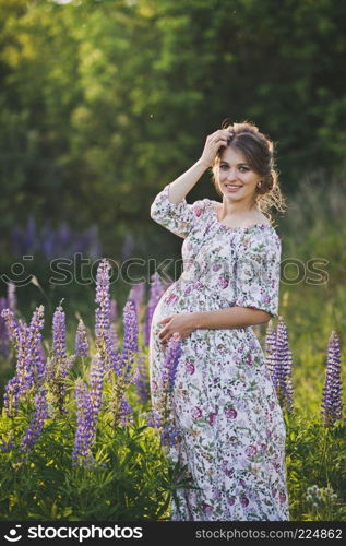 Portrait of a happy future mother against the background of Lupin field.. Portrait in full growth of the girl on the background of the field of lupine