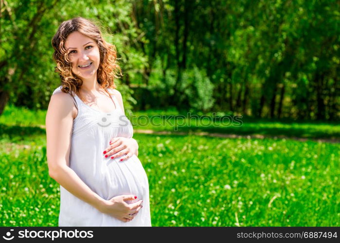 Portrait of a happy future mother in anticipation of a child in a green park