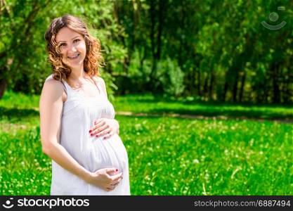 Portrait of a happy future mother in anticipation of a child in a green park