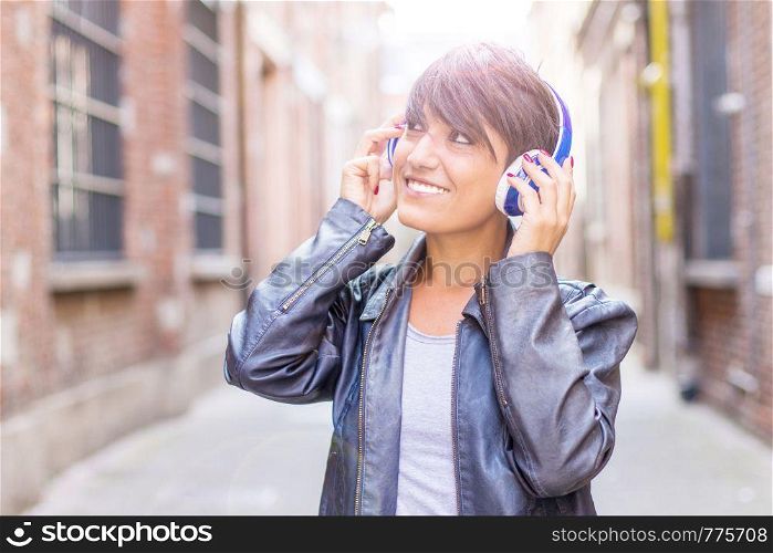 Portrait of a happy girl listening music with wireless headphones in the street