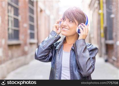 Portrait of a happy girl listening music with wireless headphones in the street
