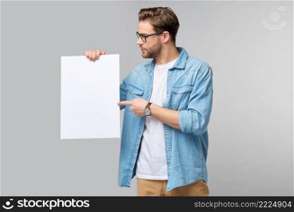 Portrait of a happy handsome young man holding blank white card or sign over white background.. Portrait of a happy handsome young man holding blank white card or sign over white background