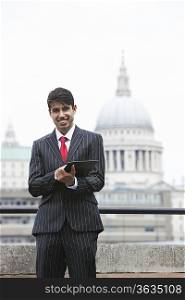 Portrait of a happy Indian businessman using tablet PC against St. Paul&acute;s Cathedral