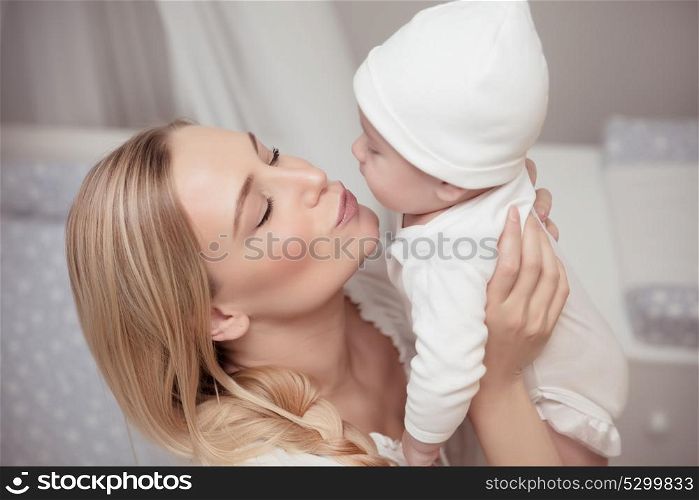 Portrait of a happy mother kissing her cute little child, with pleasure spending time at home, family love, new life concept