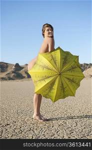 Portrait of a happy naked woman with yellow umbrella on barren landscape