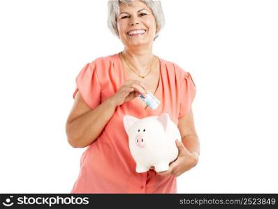 Portrait of a happy old woman putting money on a piggy bank, isolated on a white background