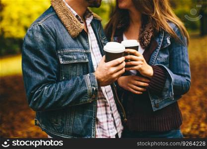 Portrait of a happy romantic couple with coffee walking outdoors in the autumn park