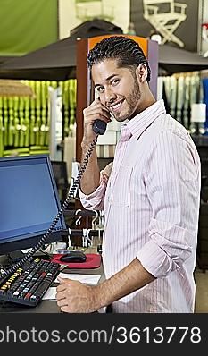 Portrait of a happy salesperson listening to telephone receiver in store