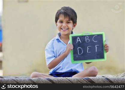 Portrait of a happy school boy holding slate with English alphabet on it
