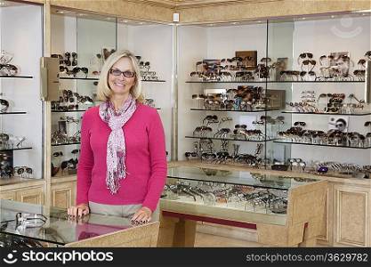 Portrait of a happy senior female optician standing in store