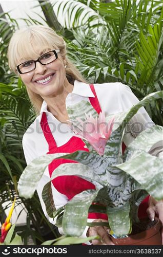 Portrait of a happy senior woman standing behind flower plant in greenhouse