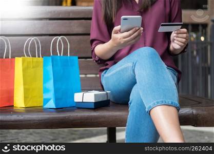 Portrait of a happy shopper paying online with credit card through smartphone with bags in a mall