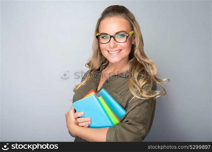 Portrait of a happy smiling student girl with colorful books in hands over gray background, enjoying education in high school