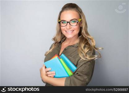 Portrait of a happy smiling student girl with colorful books in hands over gray background, enjoying education in high school