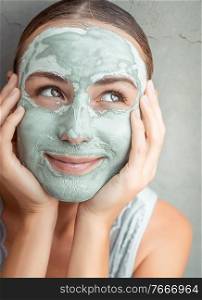 Portrait of a happy woman doing facial mask of a blue clay, at home, with pleasure touching face with her hands, p&ering and beauty treatment concept