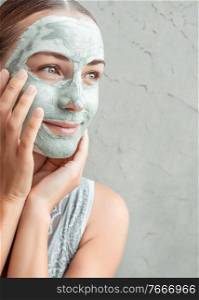 Portrait of a happy woman doing facial mask of a blue clay, with pleasure touching face with her hands, p&ering and beauty treatment concept