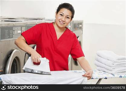Portrait of a happy woman employee in red uniform ironing clothes in Laundromat