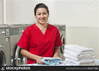 Portrait of a happy woman in red uniform with towel in Laundromat