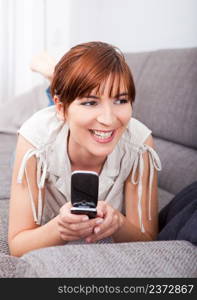 Portrait of a happy woman lying on sofa, sending a sms