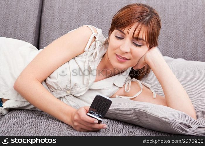 Portrait of a happy woman lying on sofa, sending a sms
