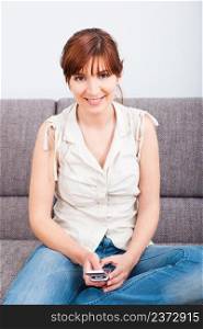 Portrait of a happy woman sitting on sofa and holding a cellphone