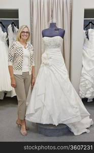 Portrait of a happy woman standing by elegant bridal dress in boutique