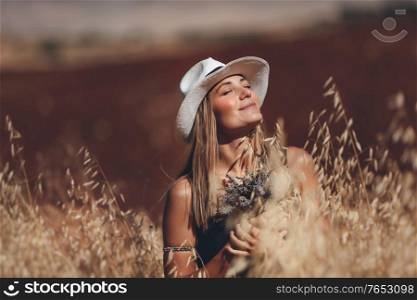 Portrait of a Happy Young Blond Woman Outdoors. Girl Holding Lavender Flowers Bouquet. Standing in a Wheat Field. Enjoying Nature. Beautiful Sunny Day.