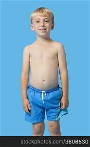 Portrait of a happy young boy in swim trunks over blue background