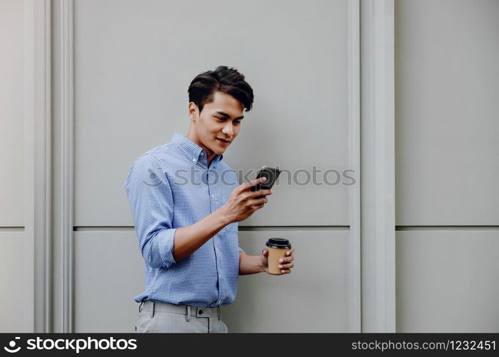 Portrait of a Happy Young Businessman Using Mobile Phone. Lifestyle of Modern People. Standing by the Wall with Coffee Cup