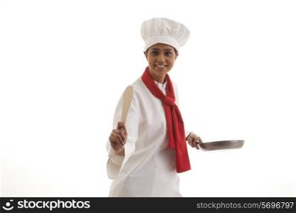 Portrait of a happy young chef holding frying pan and wooden spatula isolated over white background