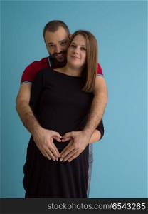 Portrait of a happy young couple,man holding his pregnant wife belly isolated over blue background. pregnant couple isolated over blue background