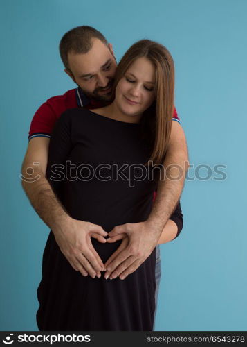 Portrait of a happy young couple,man holding his pregnant wife belly isolated over blue background. pregnant couple isolated over blue background