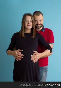 Portrait of a happy young couple,man holding his pregnant wife belly isolated over blue background. pregnant couple isolated over blue background