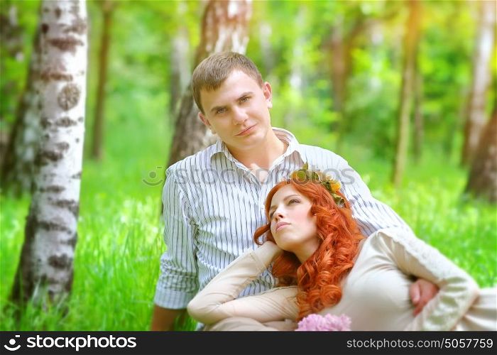Portrait of a happy young couple relaxing in the fresh green spring park, sitting on a field between birch trees, enjoying wedding day