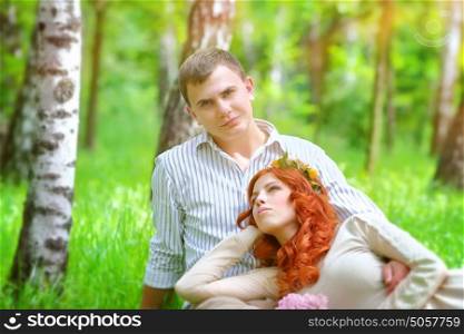 Portrait of a happy young couple relaxing in the fresh green spring park, sitting on a field between birch trees, enjoying wedding day