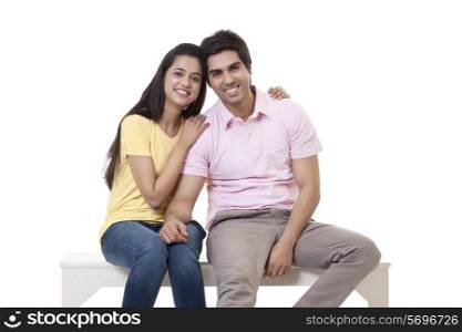 Portrait of a happy young couple sitting on bench over white background