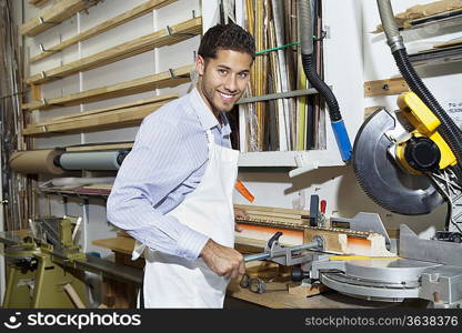 Portrait of a happy young craftsman standing by circular saw machinery