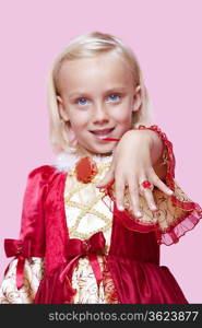 Portrait of a happy young girl dressed in princess costume displaying ring over pink background