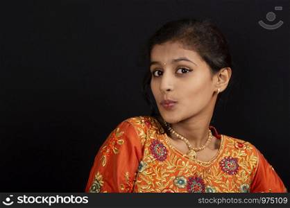 Portrait of a happy young Indian girl pursing her lips on black background