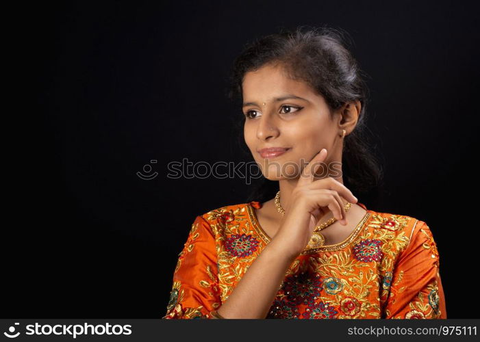 Portrait of a happy young Indian girl smiling on black background with hand on chin