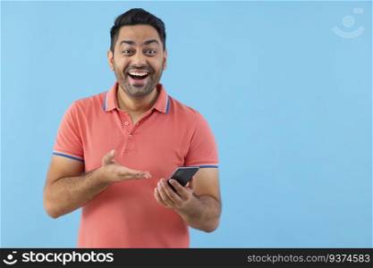 Portrait of a happy young man looking at camera and pointing at his Smartphone