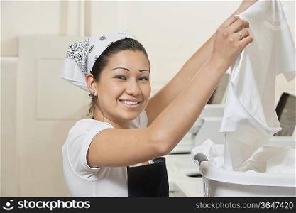 Portrait of a happy young woman holding cloth in Laundromat