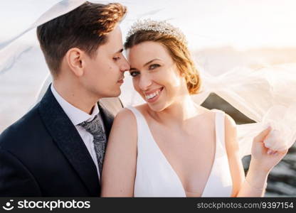 Portrait of a just married couple under the bride’s veil at sunset