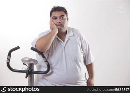 Portrait of a lazy obese man with an exercise bike over white background