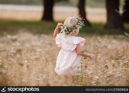 Portrait of a little beautiful girl on nature on summer day vacation. child in red dress is playing in the green grass at the sunset time. The concept of family holiday and time together. little beautiful girl on nature on summer day vacation. childgirl in panties and a flowers wreath on her head is playing in the field on summer day. The concept of family holiday and time together.