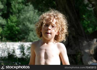 Portrait of a little blond and curly boy, outside