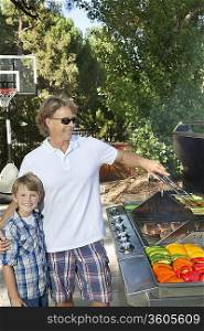 Portrait of a little boy with father barbecuing vegetable on barbecue grill in lawn