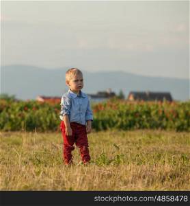 Portrait of a little cute boy in red pants on a rural background. Outdoor portrait of a cute little boy