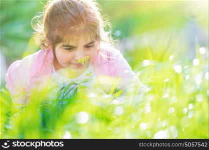 Portrait of a little dreamy girl having fun outdoors in nice sunny day, enjoying aroma of a little flower on the backyard